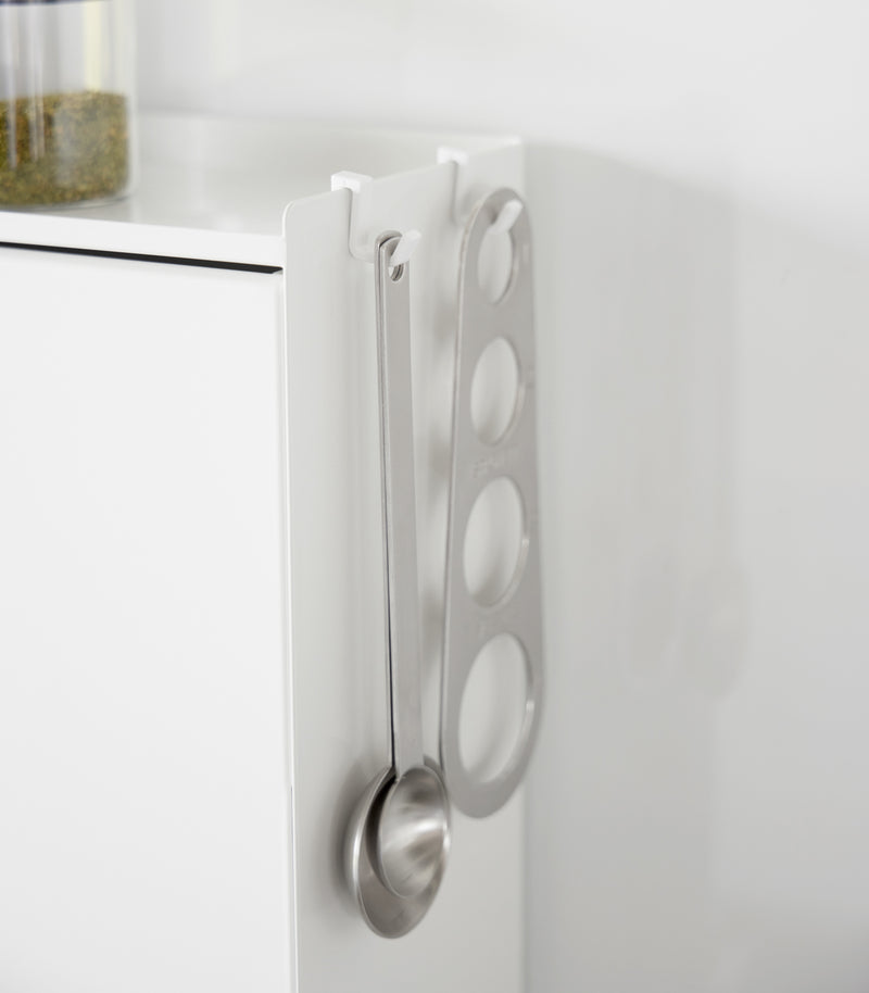 A close-up image of kitchen utensils hanging from hooks placed along the top ridge of the Concealable Spice Rack by Yamazaki Home in white.