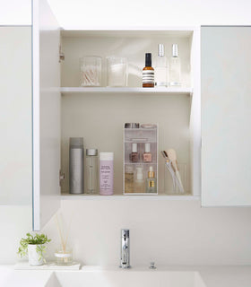 A white medicine cabinet is open to display the inside contents. Sunlight is focused on the right upper corner. Below is a bathroom sink. view 23