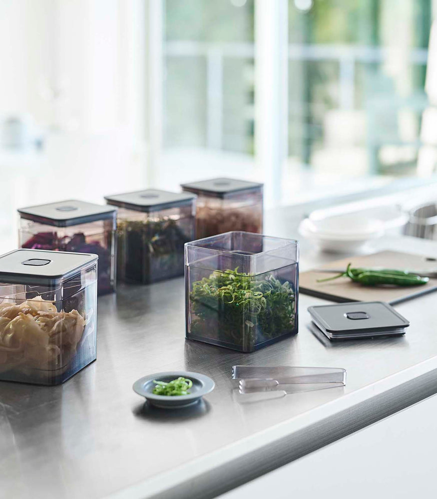 View 9 - Black Vacuum-Sealing Food Container w. Tongs holding scallions on kitchen countertop by Yamazaki Home.