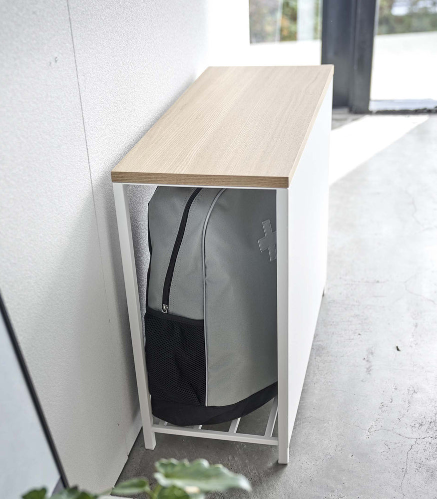 View 5 - Side view of white Yamazaki Discreet Entryway Storage Shelf against a wall with a backpack inside