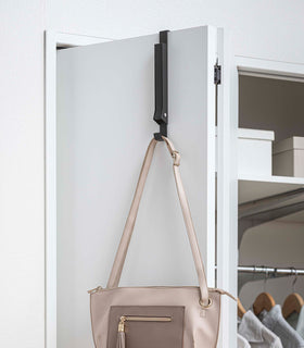 Black Yamazaki Home Folding Over-The-Door Hanger closed with a single purse hung view 24