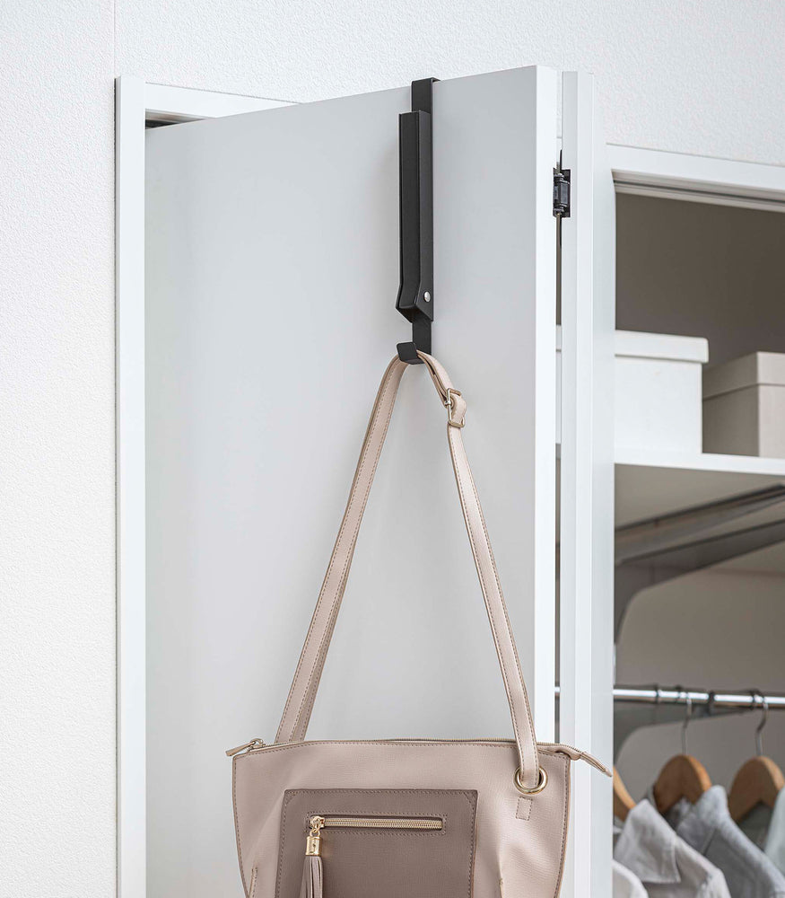 View 14 - Black Yamazaki Home Folding Over-The-Door Hanger closed with a single purse hung