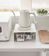 White Yamazaki Home Stackable Countertop Shelf with a basket of tea underneath and a kettle above