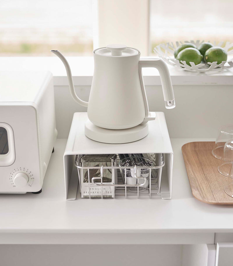 White Yamazaki Home Stackable Countertop Shelf with a basket of tea underneath and a kettle above
