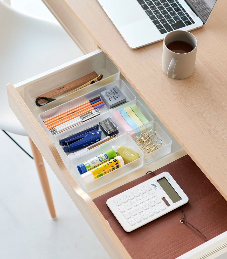 View 51 - Three different sizes of stackable clear organizers—small, medium, and large—are neatly placed in a desk drawer. Made from transparent material, they accommodate stationery items like pens, paper clips, and sticky notes, showcasing their clarity and stackability.