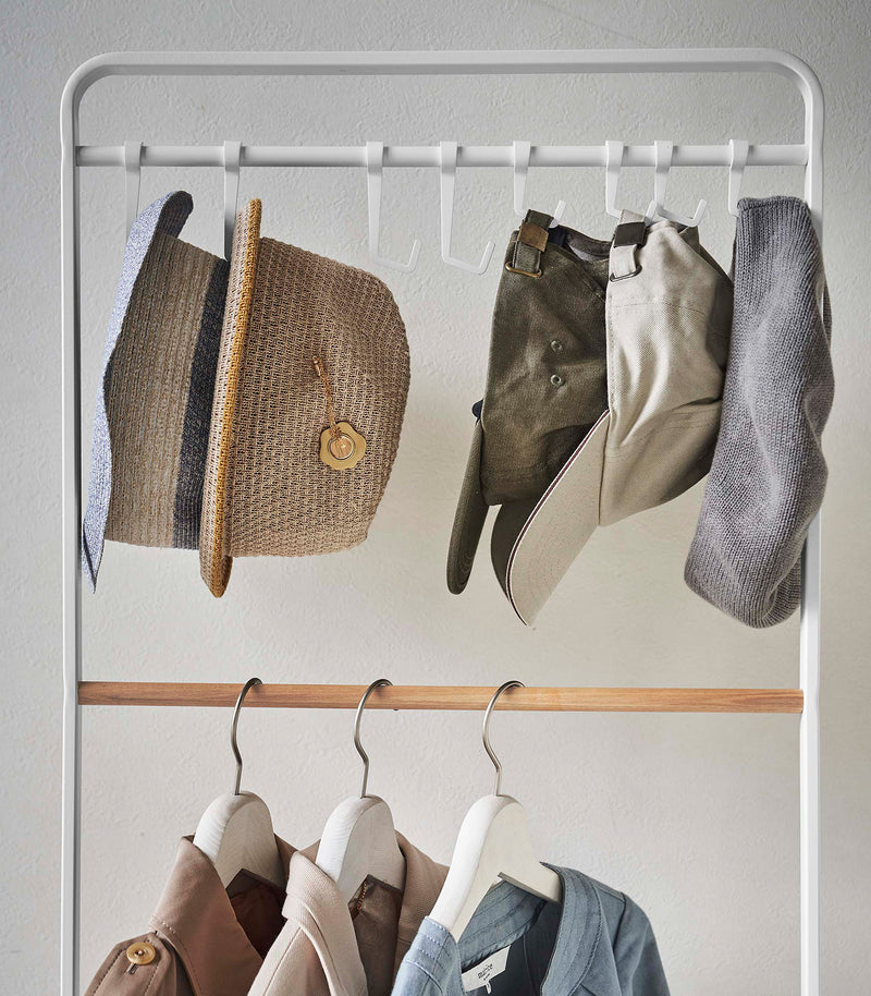 Frontal close up of hats hung on hooks included with white Yamazaki Home Coat Rack with Hat Storage