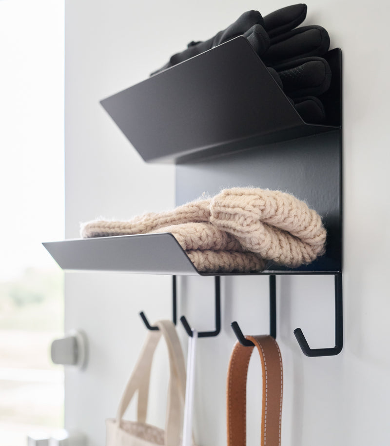 Close-up of the shelves on the Magnetic Entryway Rack by Yamazaki Home in black. Various entryway items are stored on the rack including gloves and a dog leash.