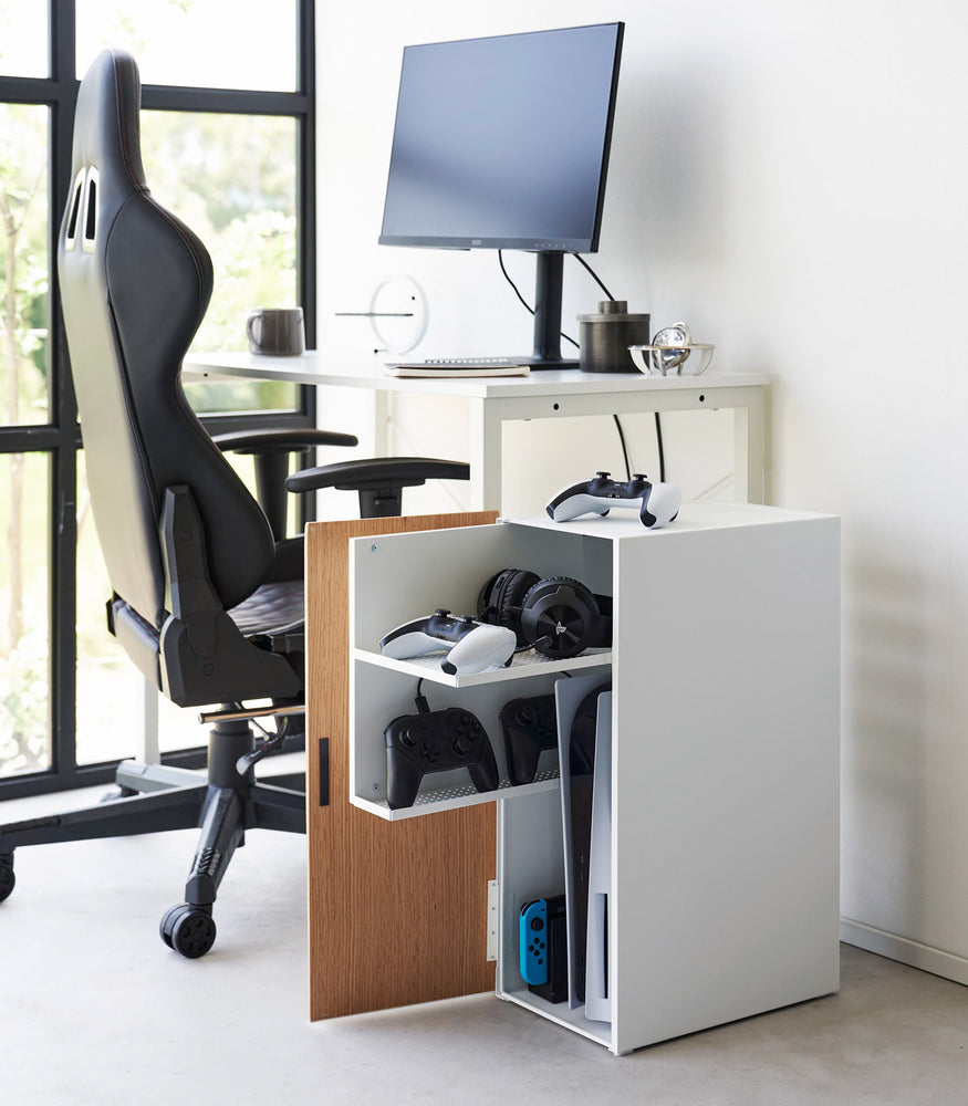 View 7 - The white video game storage cabinet is placed next to the home office desk. With the door opened, it showcases video games, controllers, and headsets neatly organized inside, demonstrating its functionality and seamless integration into the room's decor