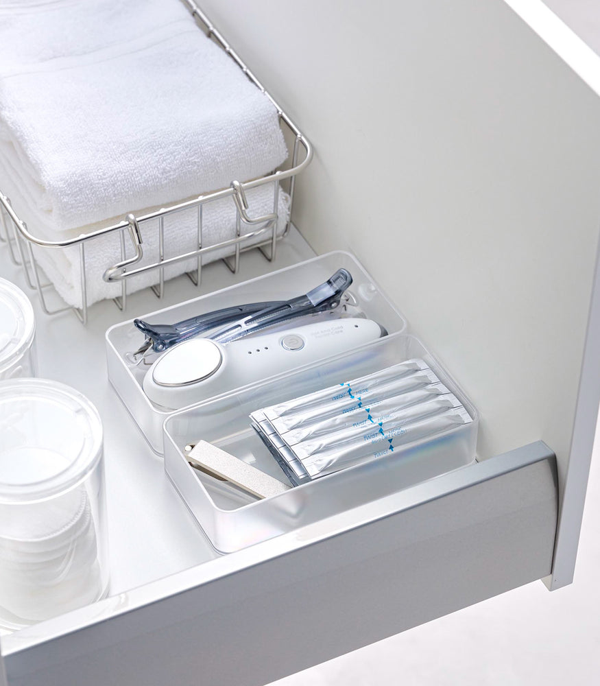 View 17 - Two medium stackable clear organizers are placed in a bathroom drawer, organizing hair clips, a face machine, and sanitary goods