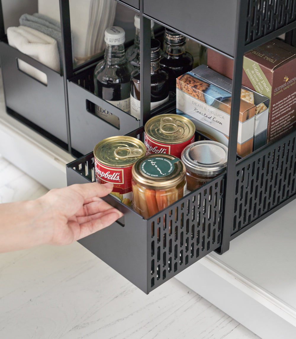 Three two-tier black storage bins are displayed in a lower cabinet. Both levels of each hold various food products. A model is sliding the lower level of one out to show its accessibility.