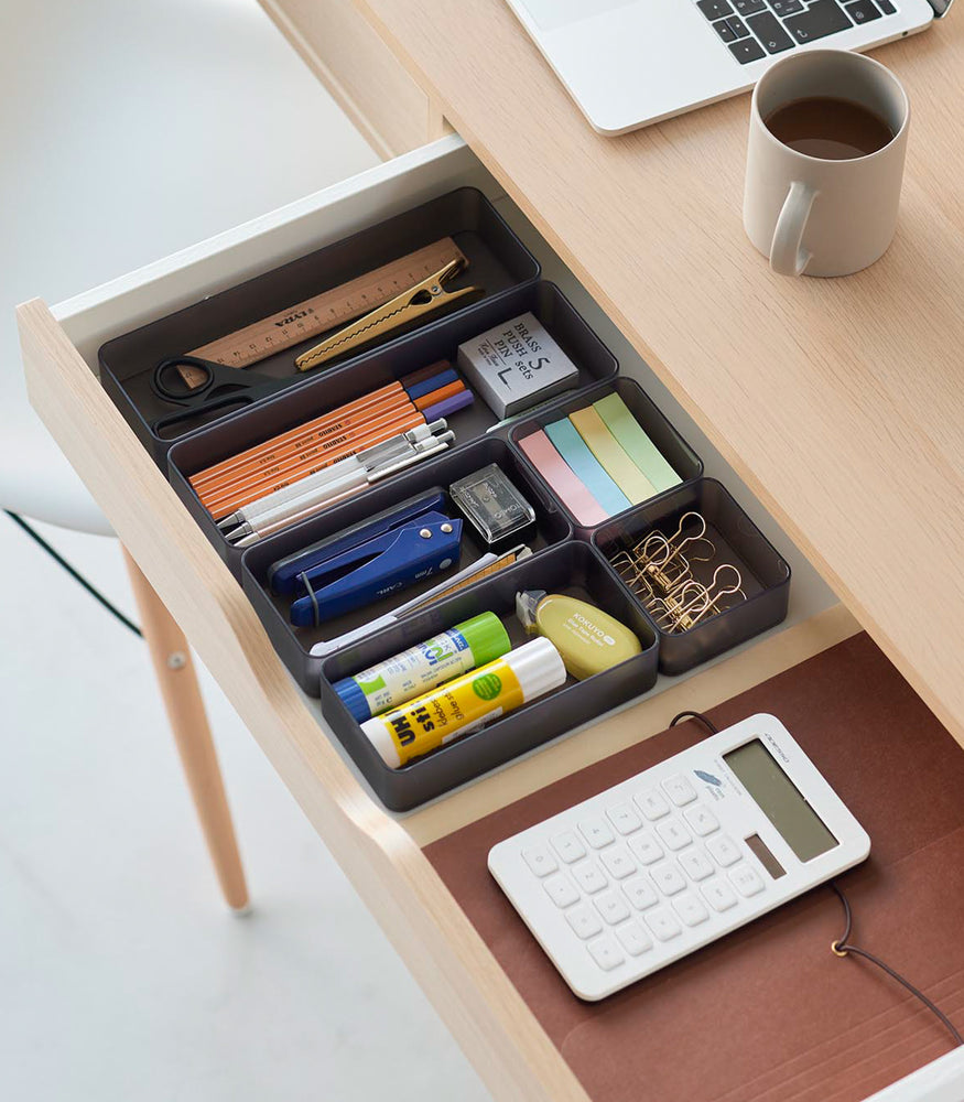 View 28 - Three different sizes of stackable clear organizers in black —small, medium, and large—are neatly placed in a desk drawer. Made from transparent material, they accommodate stationery items like pens, paper clips, and sticky notes, showcasing their clarity and stackability.