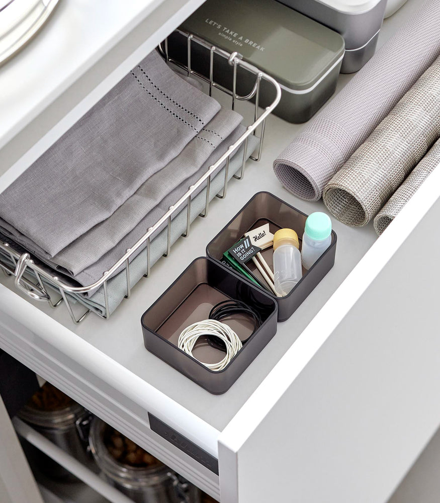 View 10 - Two small stackable clear organizers in black are placed in a kitchen drawer, organizing small items like strings and tiny sauce bottles