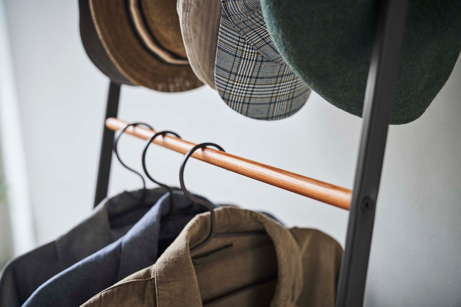 View 15 - Close up of clothes hung on black Yamazaki Home Coat Rack with Hat Storage