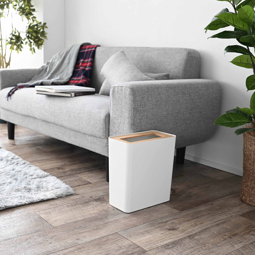 White rectangle Trash Can sitting next to a couch in the living room by Yamazaki Home.