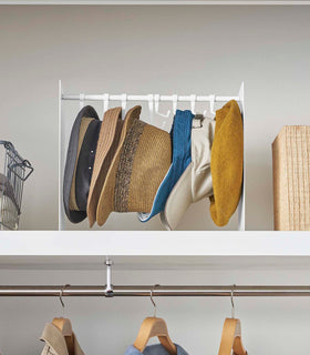 Frontal view of shortened white Yamazaki Home hat rack hanging a variety of hats in a closet view 7