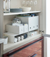 White Yamazaki Home Shelf Risers in a cabinet containing water bottles and wrap boxes