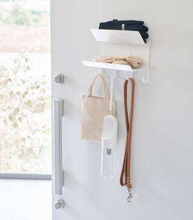 Magnetic Entryway Rack by Yamazaki Home in white mounted on a door. Gloves, a dog leash, and other entryway items are on the rack. view 2