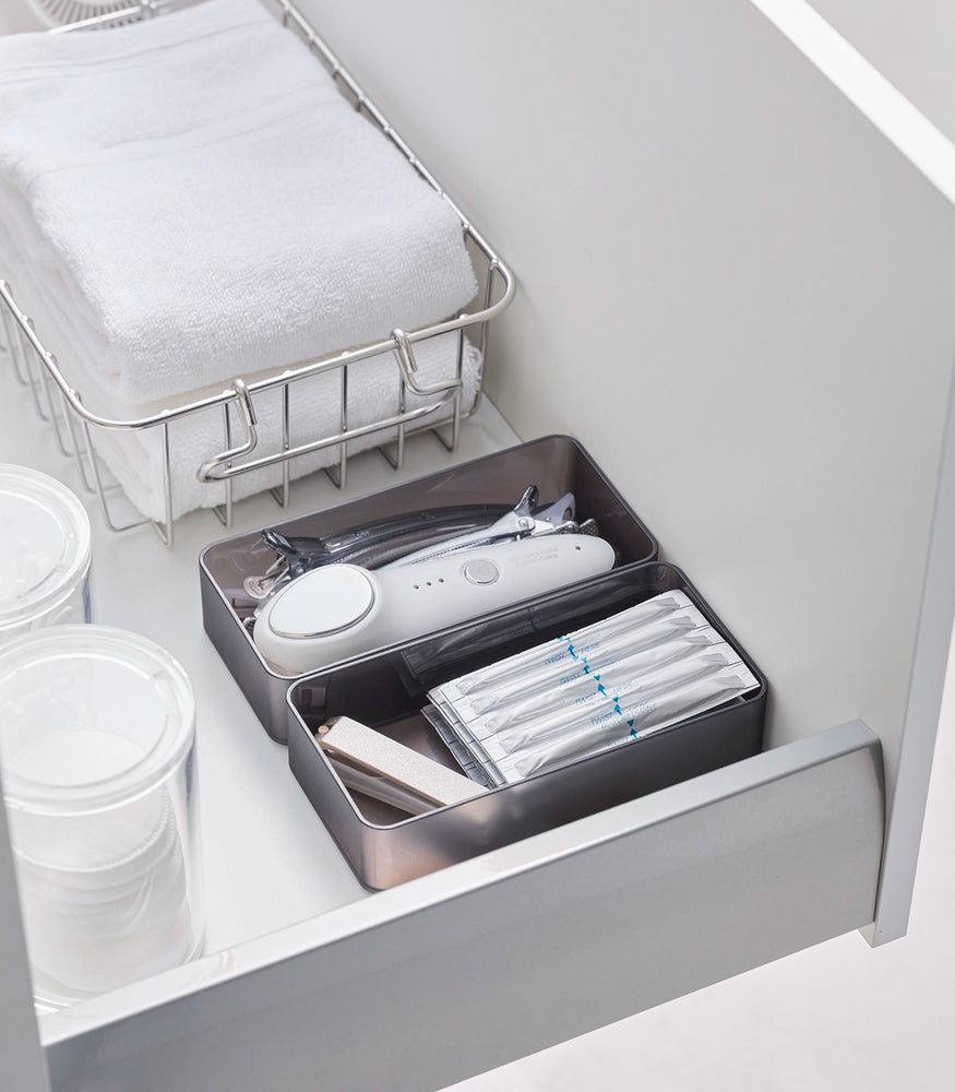 View 26 - Two medium stackable clear organizers in black are placed in a bathroom drawer, organizing hair clips, a face machine, and sanitary goods