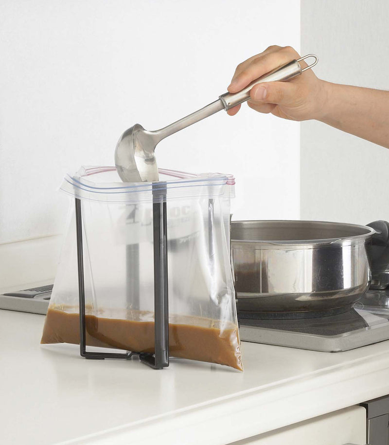 Small black Yamazaki Collapsible Bottle Dryer in a kitchen holding a bag to ladle gravy