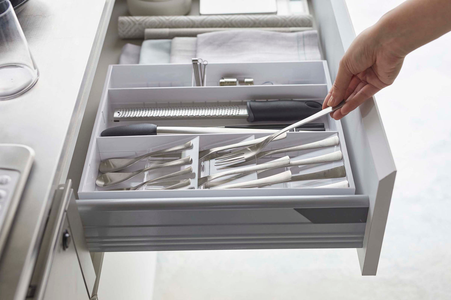 View 17 - Side view of person placing fork in white Expandable Cutlery Storage Organizer by Yamazaki Home.