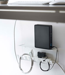 Under-Desk Cable Organizer in white by Yamazaki Home holding a power strip and router under a desk. view 4