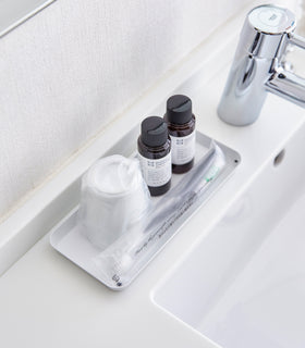 Aerial view of flat white Accessory Tray holding soap, cup, and toothbrush on bathroom sink counter by Yamazaki Home. view 14