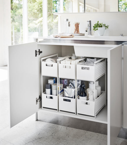 Three white two-tier storage bins are displayed in an under-a-sink cabinet. Both levels of each hold various cleaning products and supplies.