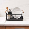 Black steel dish drying rack with wood handles on a drying tray in a modern kitchen with marble countertop near a sink from Yamazaki Home.