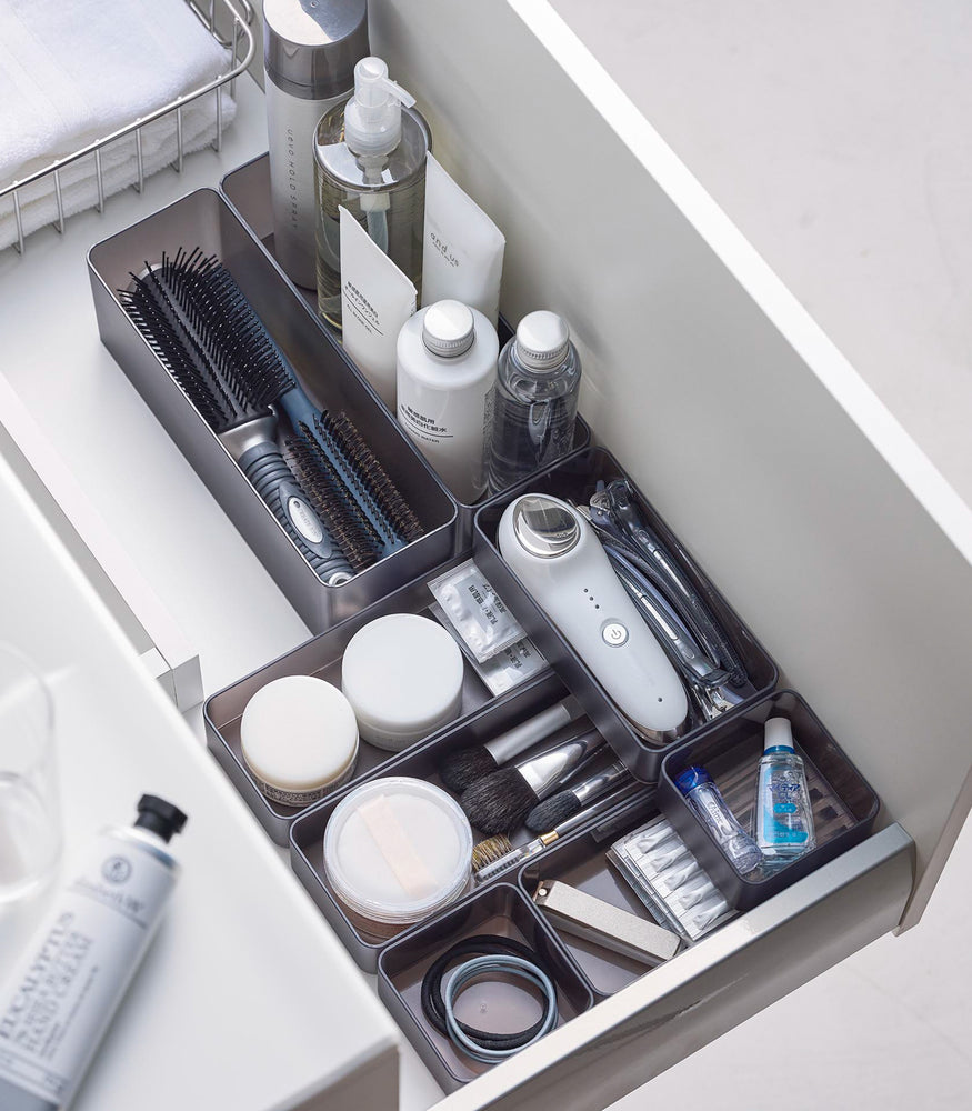 View 30 - Four different sizes of stackable clear organizers in black—small, medium, large, and deep—are neatly placed in a bathroom drawer. Made from transparent material, they accommodate items like brushes and sanitary products, showcasing their clarity and stackability.