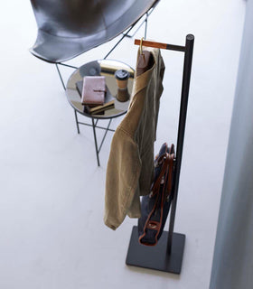Top-down view of black Yamazaki Coat Rack with a messenger bag and jacket hanging on it next to a coffee table view 13