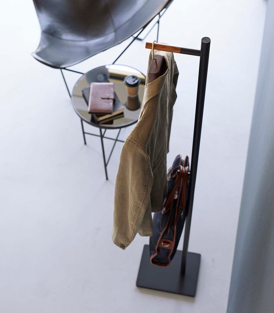 View 13 - Top-down view of black Yamazaki Coat Rack with a messenger bag and jacket hanging on it next to a coffee table
