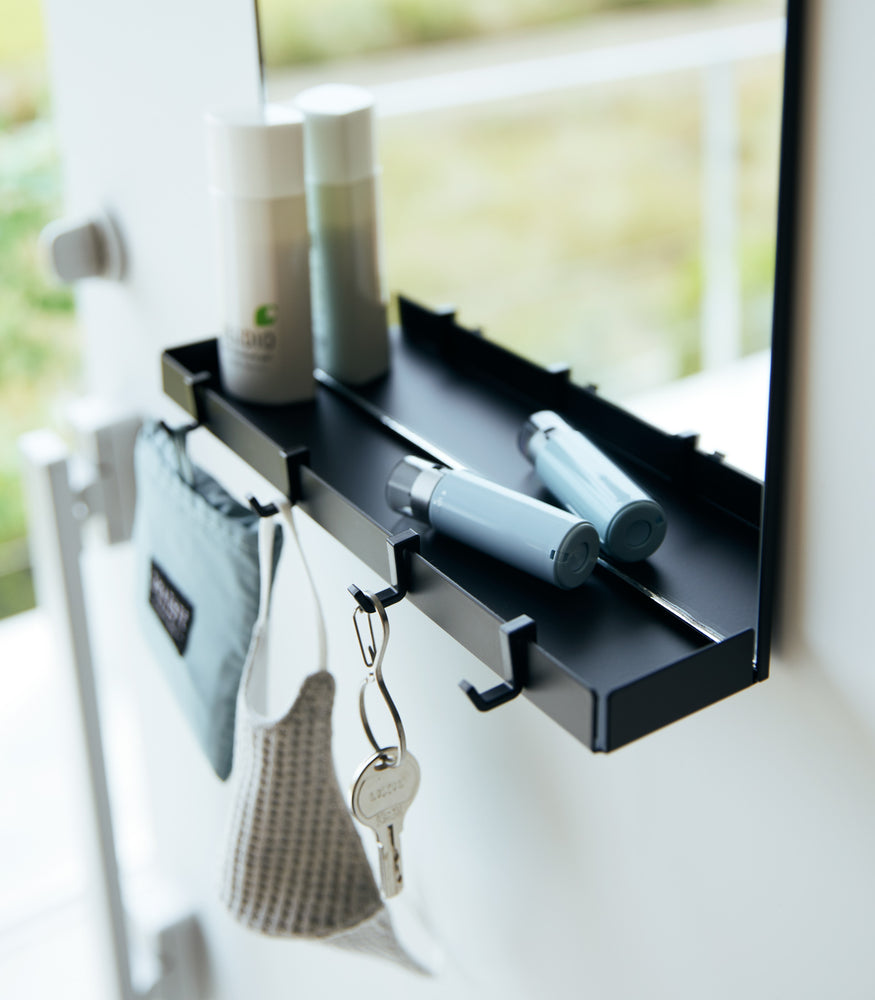 View 10 - A close up of a black Yamazaki Magnetic Mirror With Storage Rack attached to a door with a hanging bag, mask, and key.