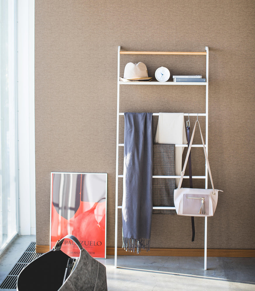 View 14 - Front view of white Leaning Ladder Rack holding clothing items and accessories by Yamazaki Home.