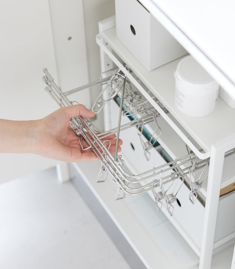 Someone is pulling out a drying hanger with clips from Yamazaki Home white Three-Tier Cabinet Storage.