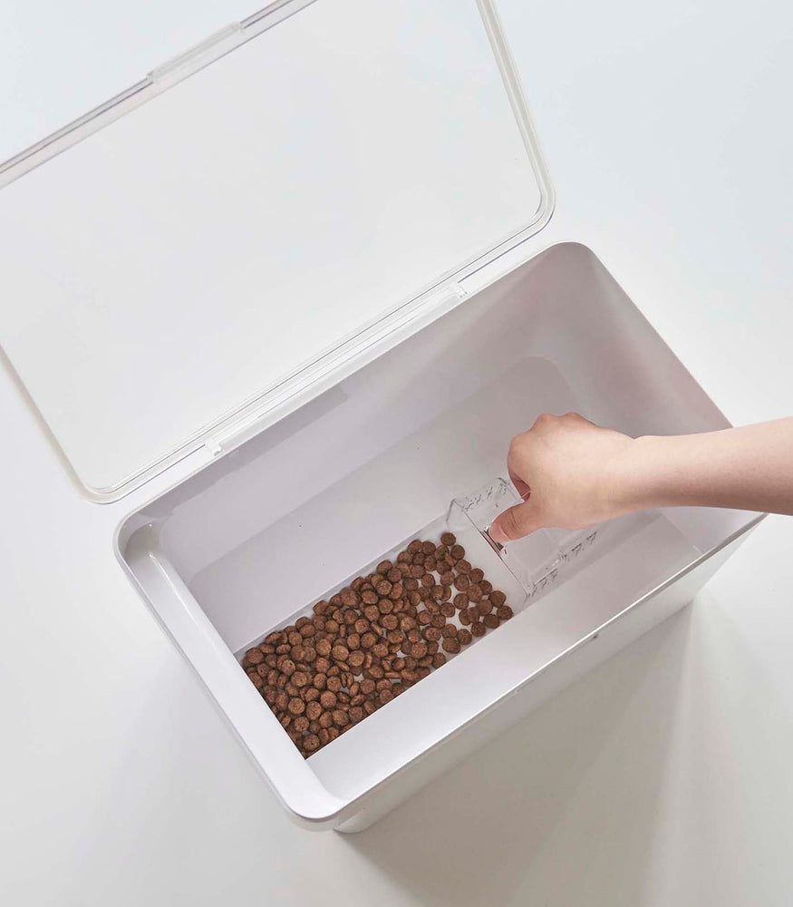 View 16 - Aerial view of person scooping pet food out of white Airtight Food Storage Container on white background by Yamazaki Home.