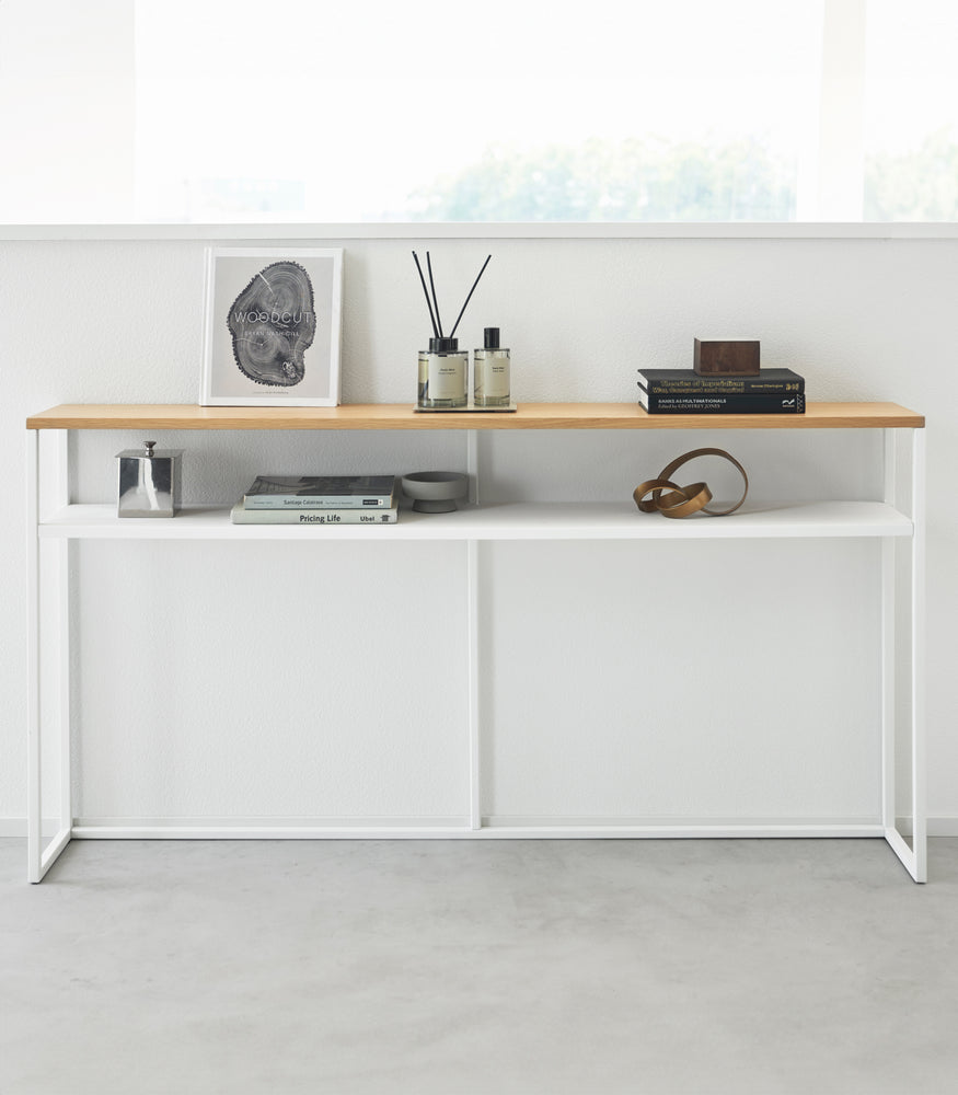 View 24 - Frontal image of white Yamazaki Home Long Console Table - Shelf against a wall with books and decorations on it
