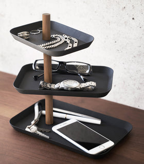 Yamazaki Home Black Rin Series 3-Tiered Accessory Tray with trays adjusted in a fan holding accessories such as a phone or glasses view 11