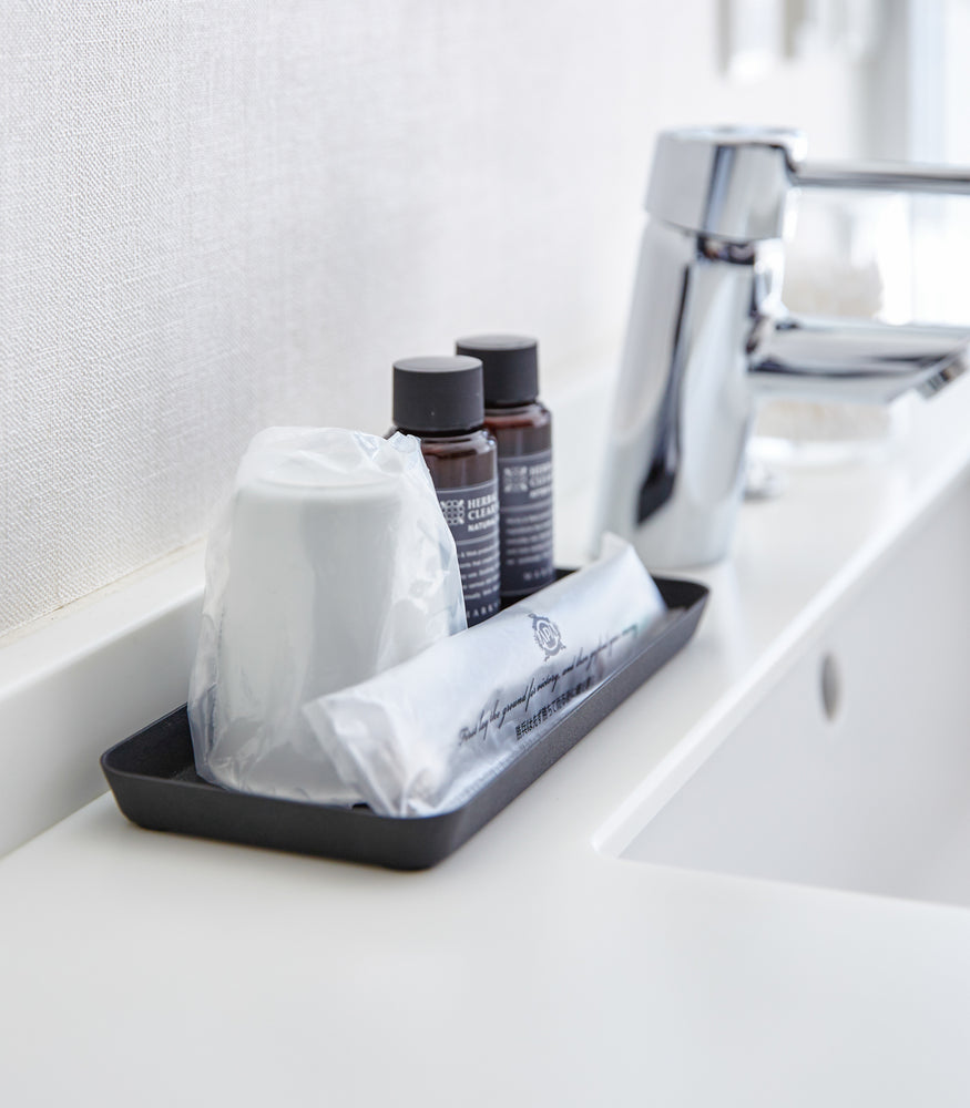View 18 - Side view of flat black Accessory Tray holding cup, soap, and toothbrush on bathroom sink counter by Yamazaki Home.