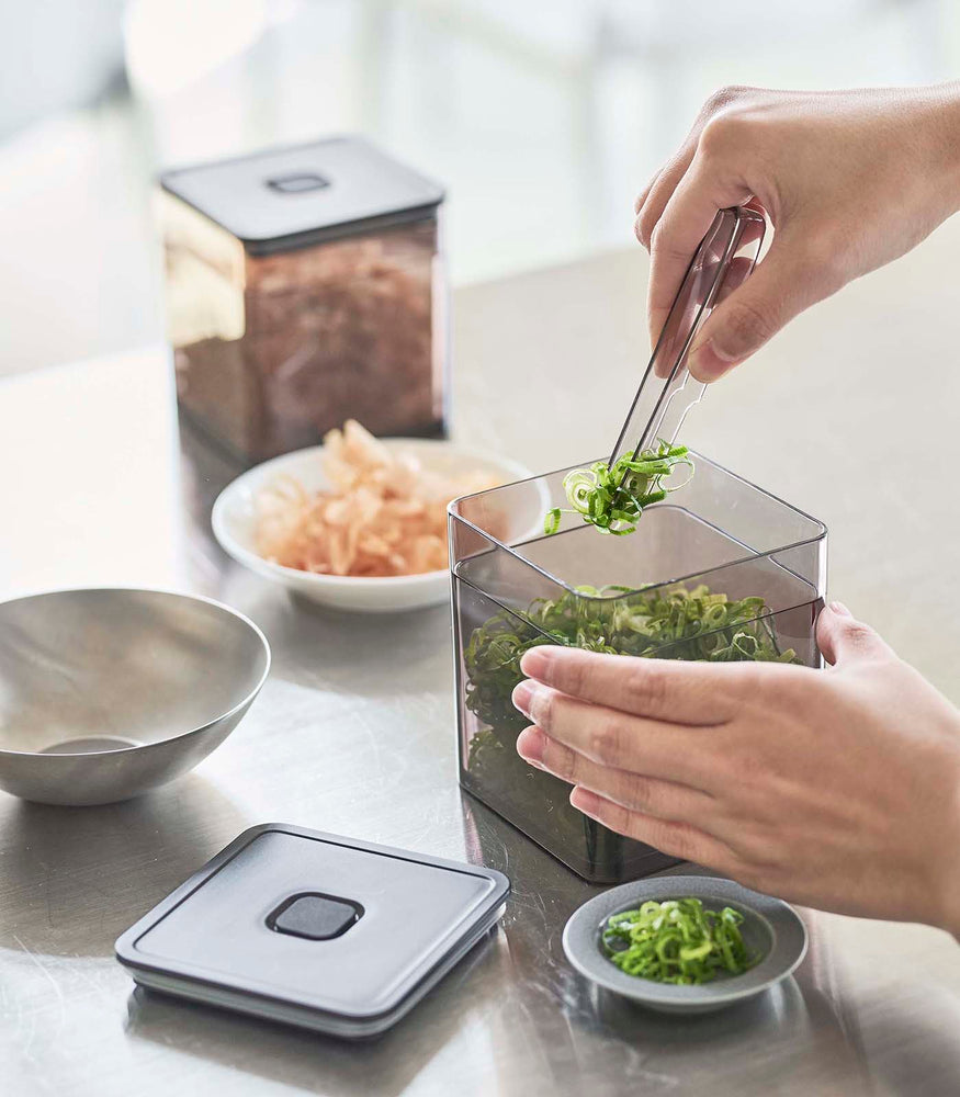 View 24 - Person using tongs to grab scallions out of black Vacuum-Sealing Food Container on kitchen countertop by Yamazaki Home.