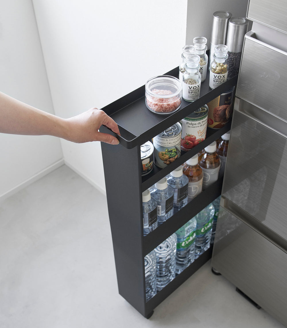 Black Yamazaki Home Slim Rolling Cart holding food and drinks being pulled out of a tight corner