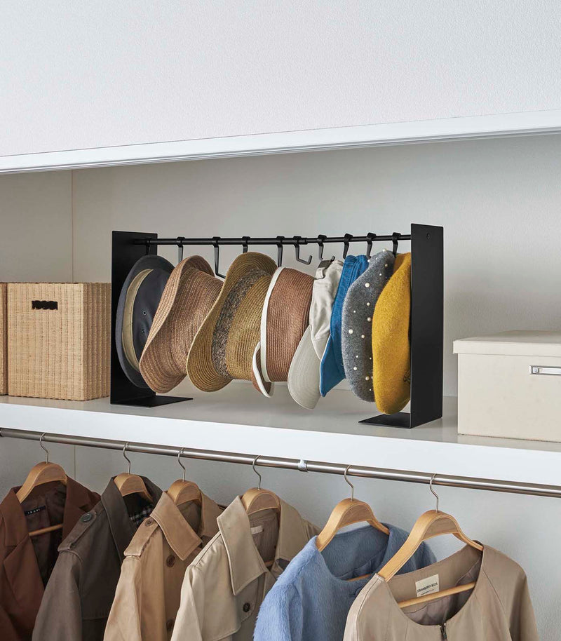 Black Yamazaki Home hat rack hanging a variety of hats in a closet