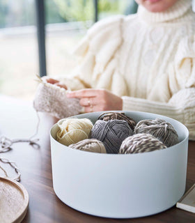 Yamazaki Home large white Storage Case with balls of yarn inside on a dining table in front of a person knitting view 16