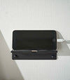 An iPhone with a charger cord plugged in is mounted on a wall. The screen is facing outward and the phone is held up on its side.
