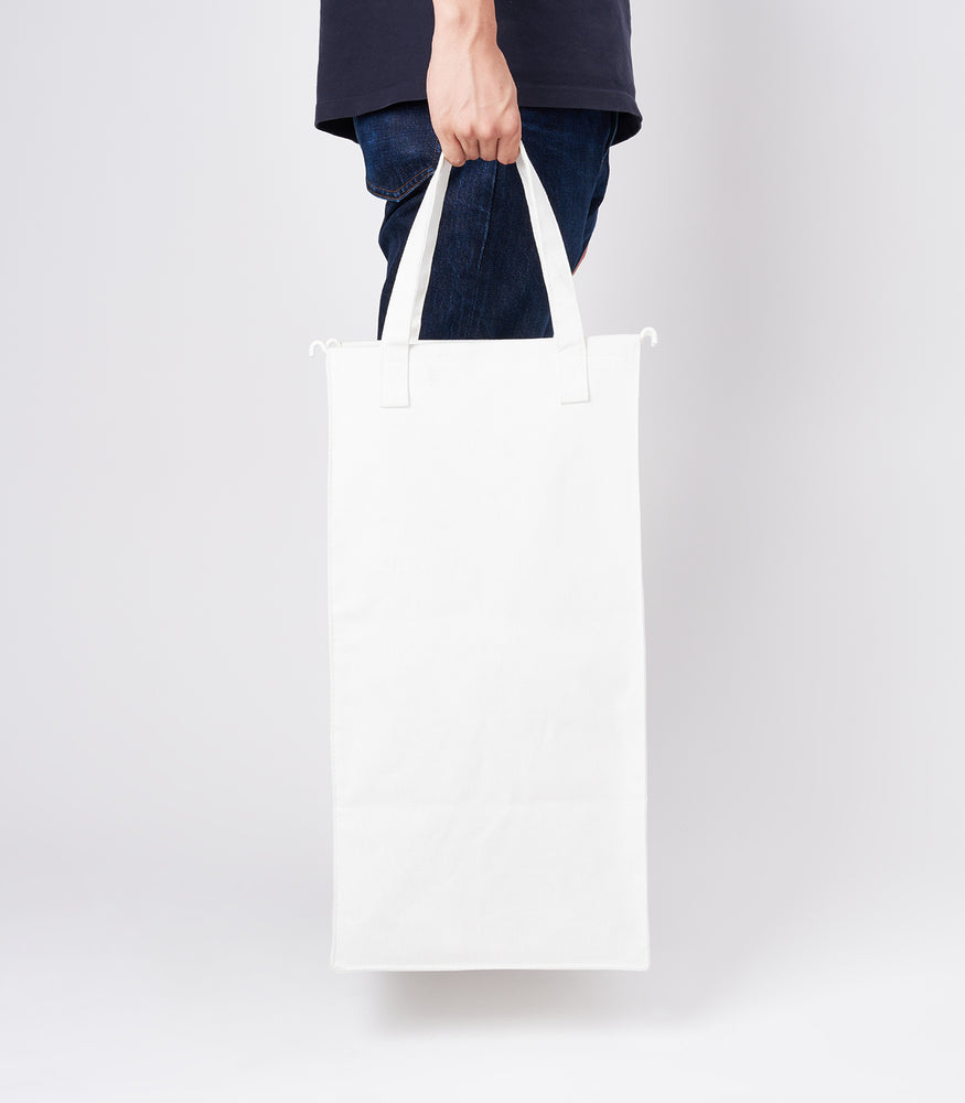 View 4 - Side view of a person holding the liner of the small Laundry Hamper with Cotton Liner in white by Yamazaki Home by the handles.
