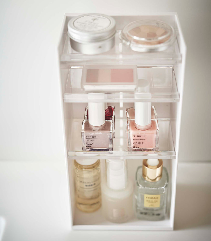 View 25 - A detailed upper view of a white rectangular cosmetics organizer sitting. The organizer has three transparent shelves with upward facing lips to prevent the products from falling-out.