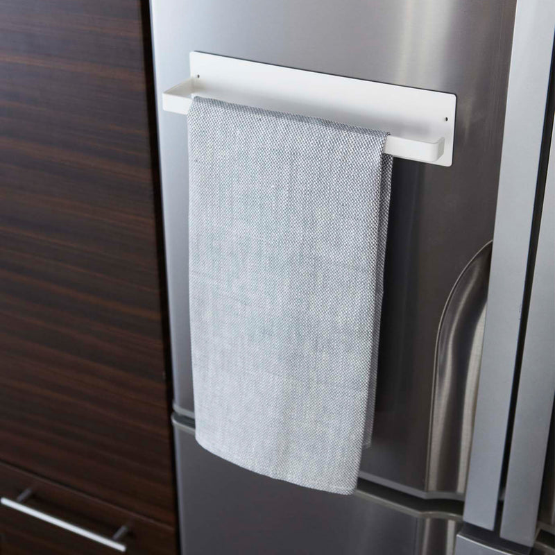 Front view of Yamazaki Home's Magnet Paper Towel Holder is seen attached to a refrigerator door with a dish towel hanging over the arm.