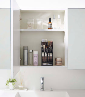 A front-facing view of an opened white medicine cabinet. Sunlight is focused on the right upper corner. The top half of the cabinet holds face serums and two clear containers with cotton swabs and rounds. view 6