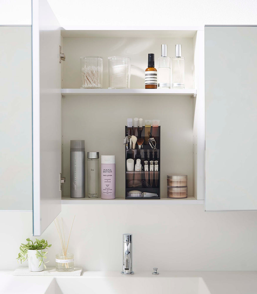 View 14 - A front-facing view of an opened white medicine cabinet. Sunlight is focused on the right upper corner. The top half of the cabinet holds face serums and two clear containers with cotton swabs and rounds.
