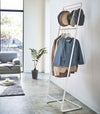 White Yamazaki Home Coat Rack with Hat Storage with hats and clothes hung on it