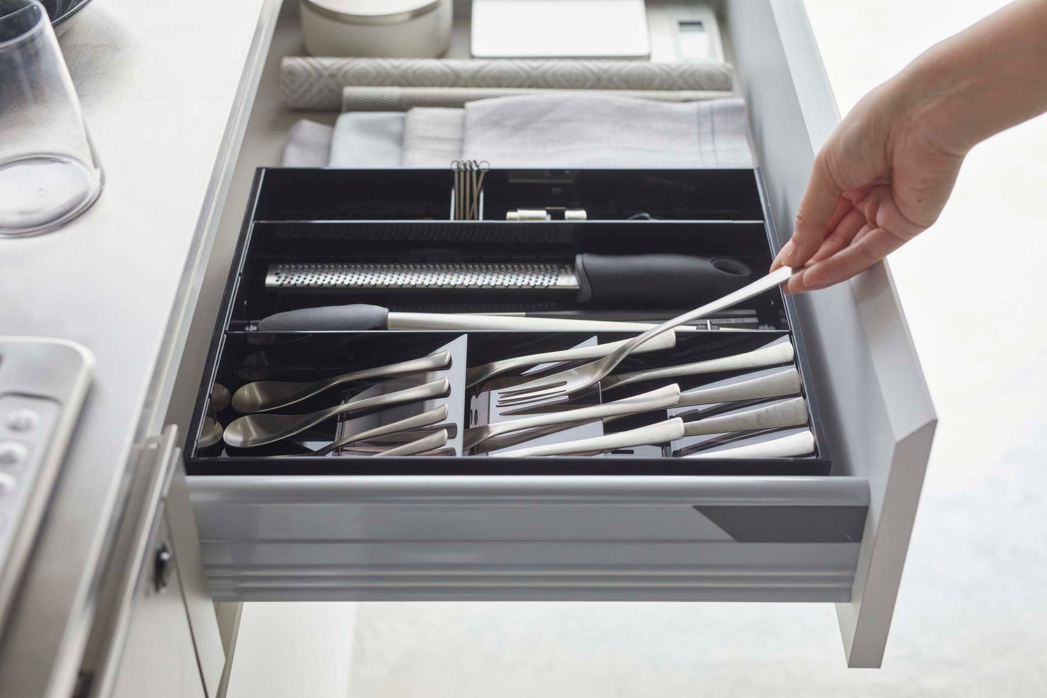 View 26 - Side view of person grabbing fork out of black Expandable Cutlery Storage Organizer by Yamazaki Home.